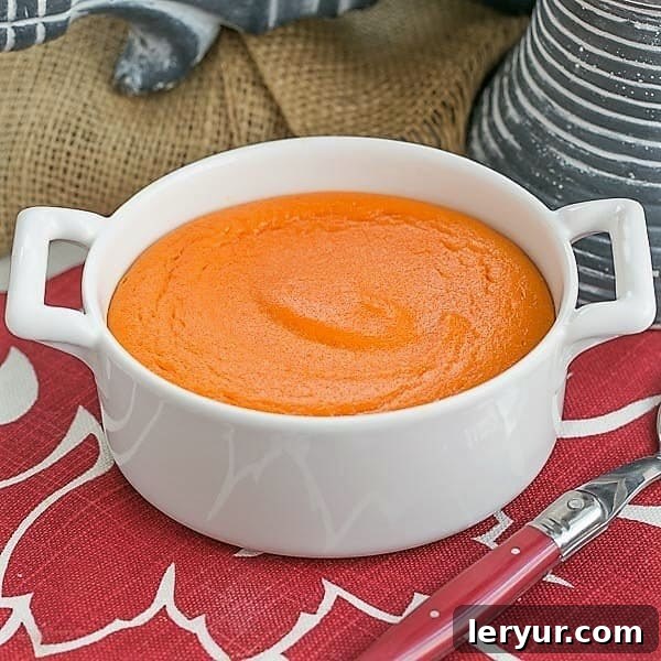 Carrot Souffle - A lovely twist for your vegetable course. Perfect for the holidays! A perfectly baked Carrot Puff in a round white baking dish, ready to serve with a red handled spoon.