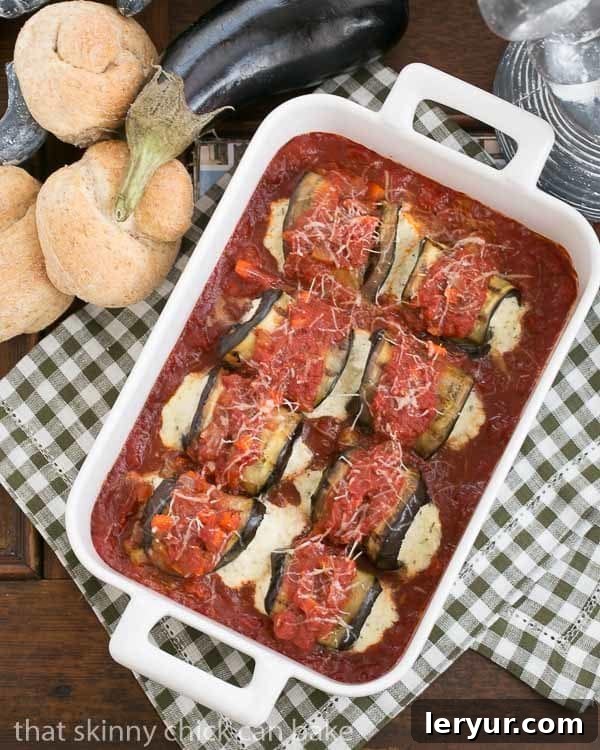 Creamy Ricotta and Mozzarella Stuffed Eggplant Rolls 3 Eggplant Rollatini baked in a white casserole dish, surrounded by wheat rolls and a whole eggplant