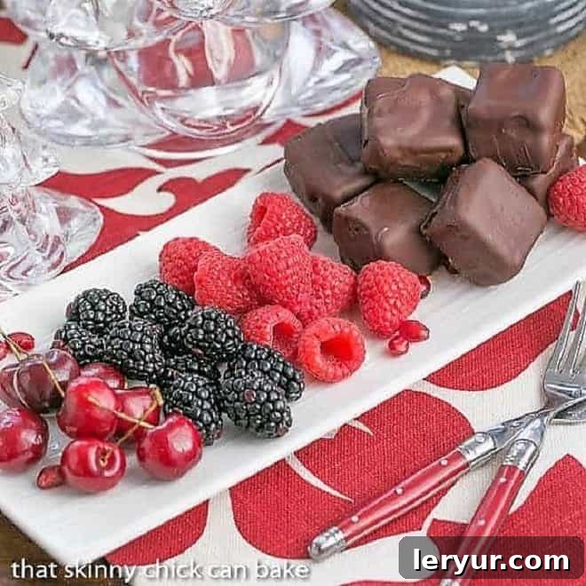 Chocolate Dipped Cheesecake Bites arranged on a pristine white tray alongside vibrant fresh fruit, showcasing their elegant presentation and tempting appeal.