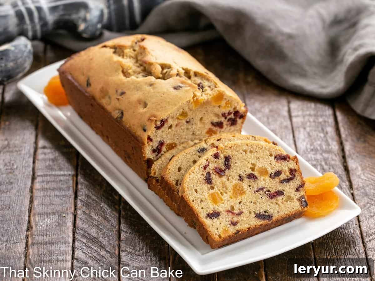 Cranberry Apricot Bread on a white tray with dried apricot garnish, highlighting its golden crust and fruit-filled interior.