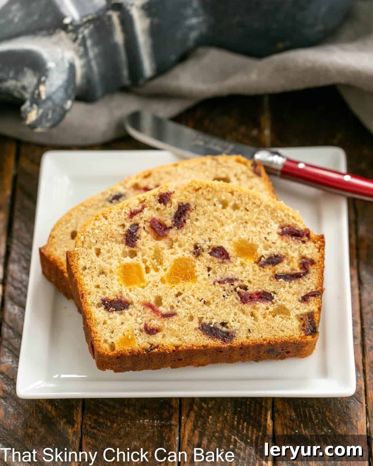Two slices of tender apricot quick bread on a square white plate, with a red-handled knife resting beside them, ready to be enjoyed.