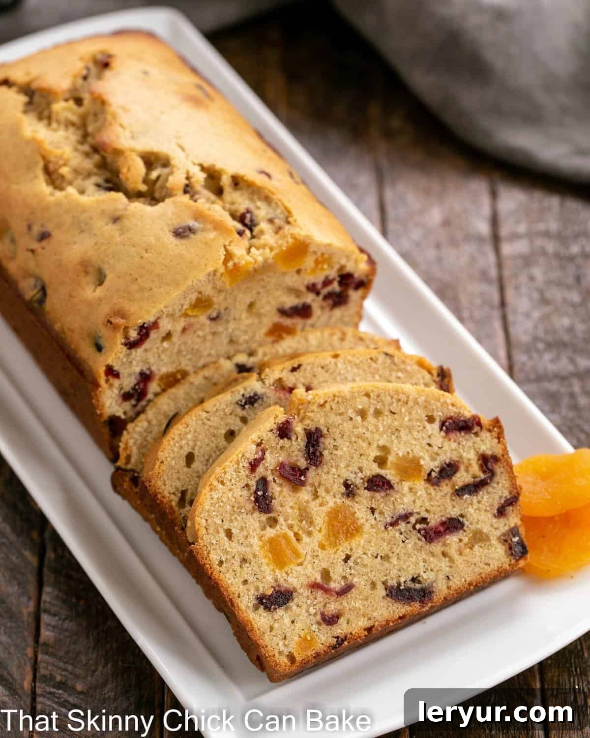 Apricot Quick Bread, partially sliced on a white tray, garnished with whole dried apricots, showcasing its moist texture.