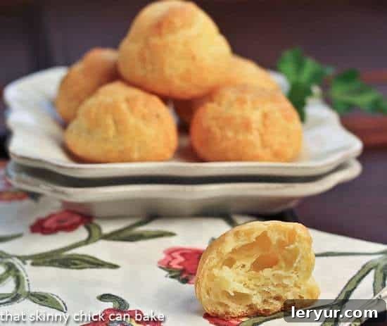 Parisian Cheese Puffs: The Ultimate Easy & Impressive Appetizer for Home Entertaining! Golden Parisian Cheese Puffs elegantly arranged on a white plate, with one puff cut in half revealing its wonderfully airy and hollow interior.