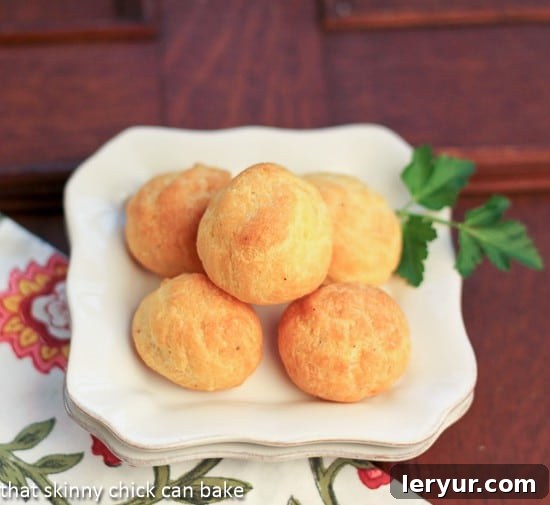 Parisian Cheese Puffs: Elegant & Easy Appetizer for Any Gathering! Overhead view of perfectly baked, golden-brown Parisian Cheese Puffs meticulously arranged on a pristine white plate, poised for serving.