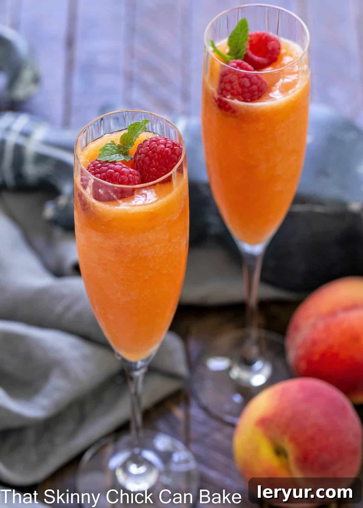 Two bellinis in elegant stemmed champagne glasses, garnished with fresh raspberries and a mint sprig.