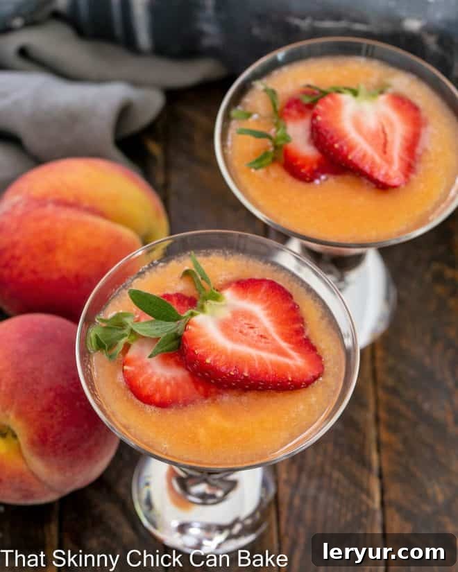An overhead view of two bellinis, garnished with fresh strawberries, next to two ripe whole peaches.
