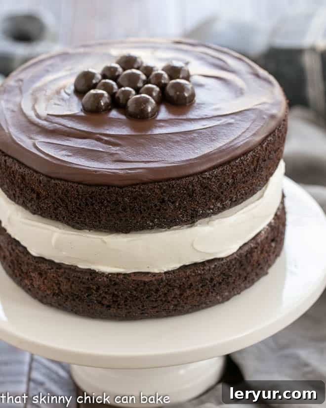 Ding Dong Cake - 2 thick moist chocolate cake layers filled with vanilla cream and topped with caramel infused ganache Ding Dong Cake topped with chocolate candies on a white cake stand.