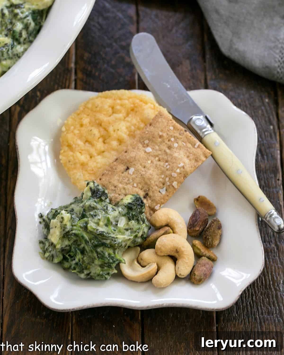 Creamy Cheesy Spinach Dip 2 Spinach and artichoke dip served on an appetizer plate with an assortment of crackers and nuts.