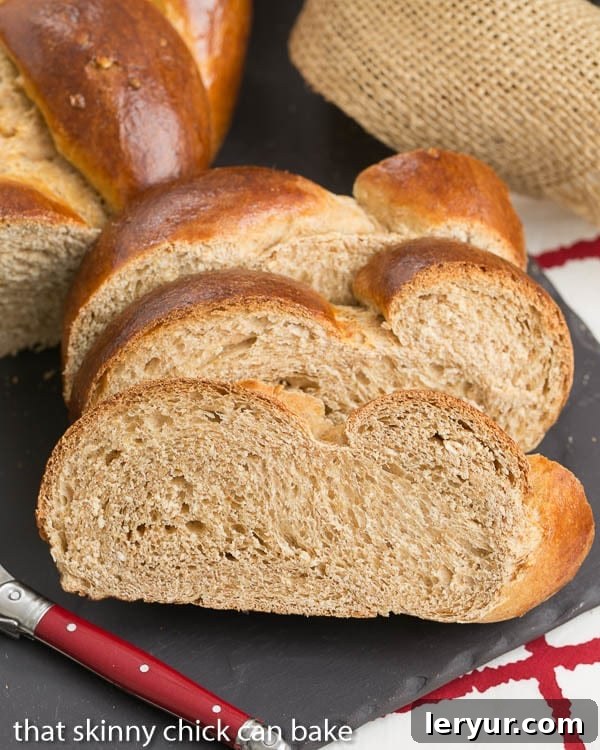 Serve your homemade Whole Wheat Challah warm with butter or use it for the best French toast. Three perfectly sliced pieces of Whole Wheat Challah on a slate tray, with a red-handled butter knife ready.