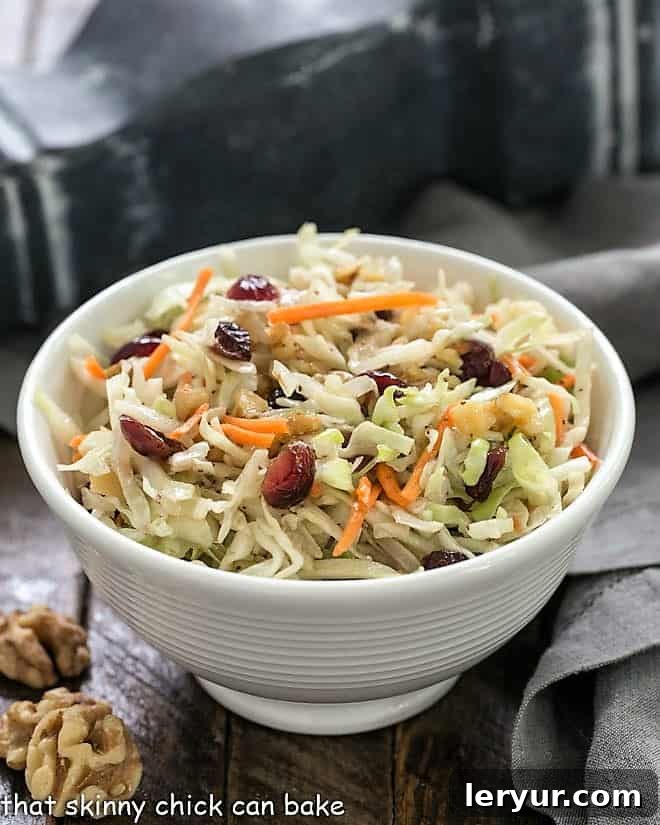This easy coleslaw recipe is quick to assemble and features a delightful mix of dried cranberries and crunchy walnuts. It's a fantastic no-mayo option for cookouts, picnics, and potluck dinners. Easy no-mayo coleslaw recipe in a small white ceramic bowl with a gray napkin and walnut halves, showcasing its fresh appeal.