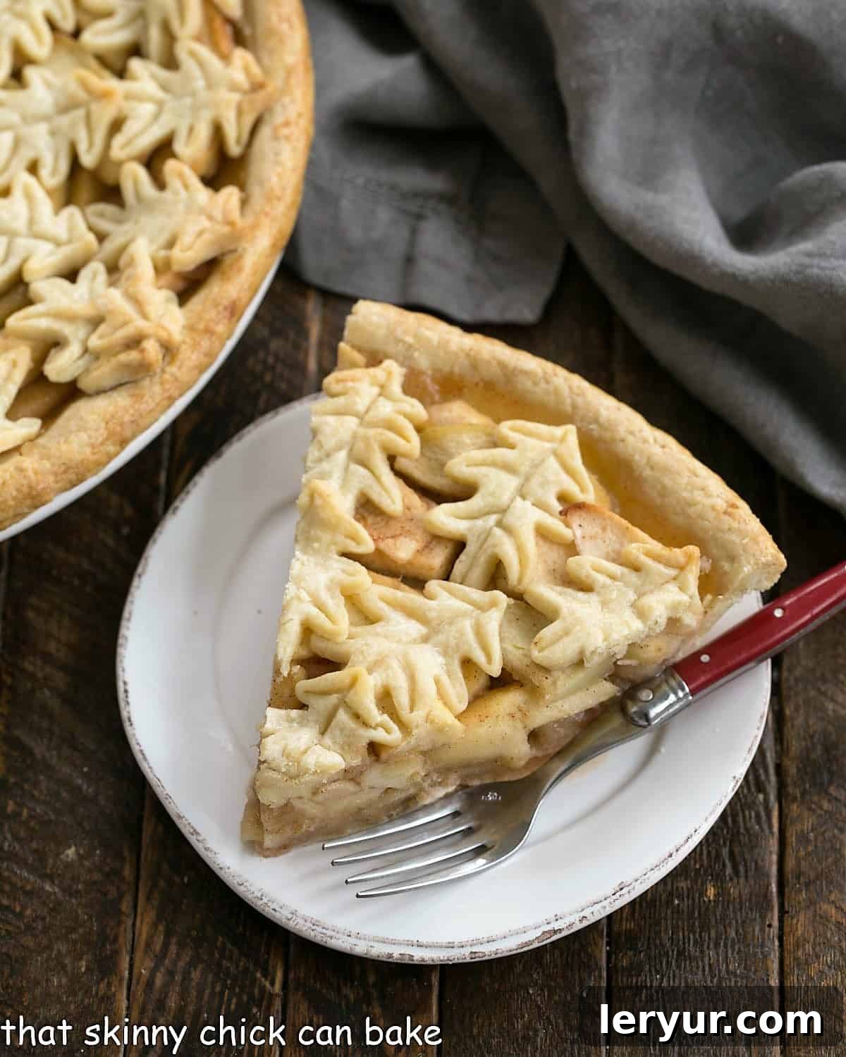 Overhead shot of a delicious slice of apple pie on a round white dessert plate, with the rest of the pie partially visible.