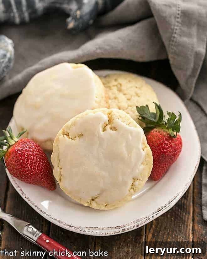 Three perfectly baked vanilla bean scones on a white plate, garnished with fresh strawberries, ready to be served with clotted cream.