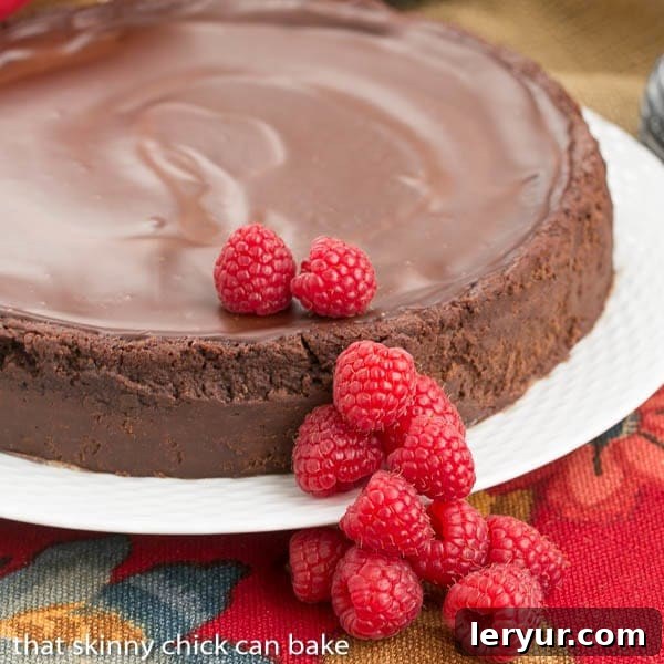 Flourless Chocolate Torte with Raspberry Sauce - A decadent gluten free flourless chocolate torte topped with chocolate ganache and berries for a beautiful finish. A stunning flourless Chocolate Torte presented on a decorative cake platter, elegantly topped with a glossy chocolate ganache and adorned with fresh raspberries, showcasing its gourmet appeal.