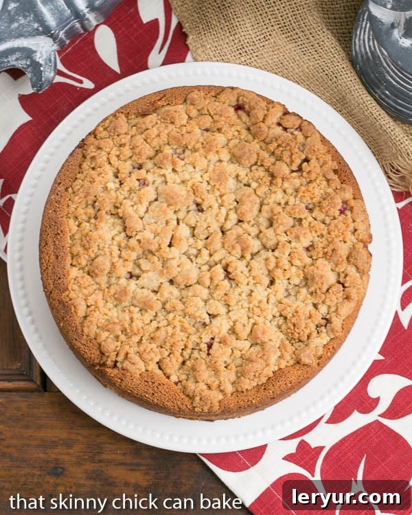 Overhead view of a whole raspberry coffee cake on a white serving plate, showing the streusel and berry distribution