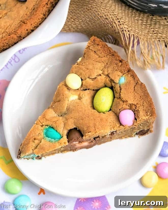 Slice of Easter cookie cake on a white dessert plate, featuring perfectly melted chocolate chips and colorful candy.