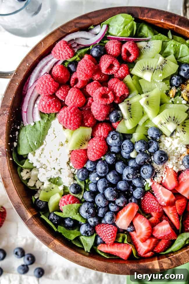 A vibrant Berry Feta Spinach Salad, beautifully topped with an assortment of fresh berries and kiwi, drizzled with a creamy strawberry poppy seed dressing.