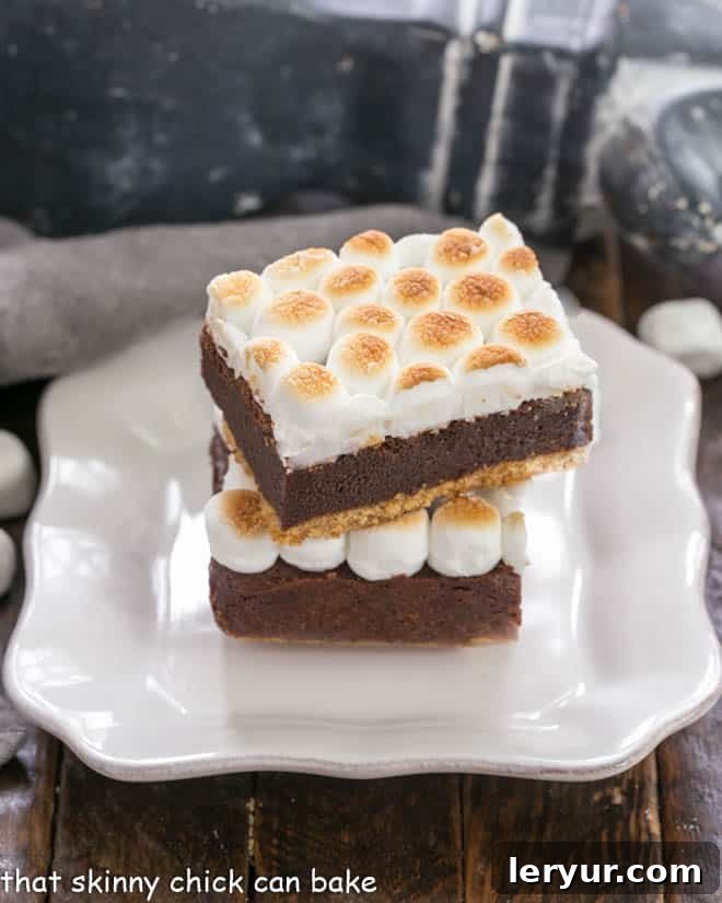 Two s'mores bars stacked on a square white plate, showcasing their distinct layers.