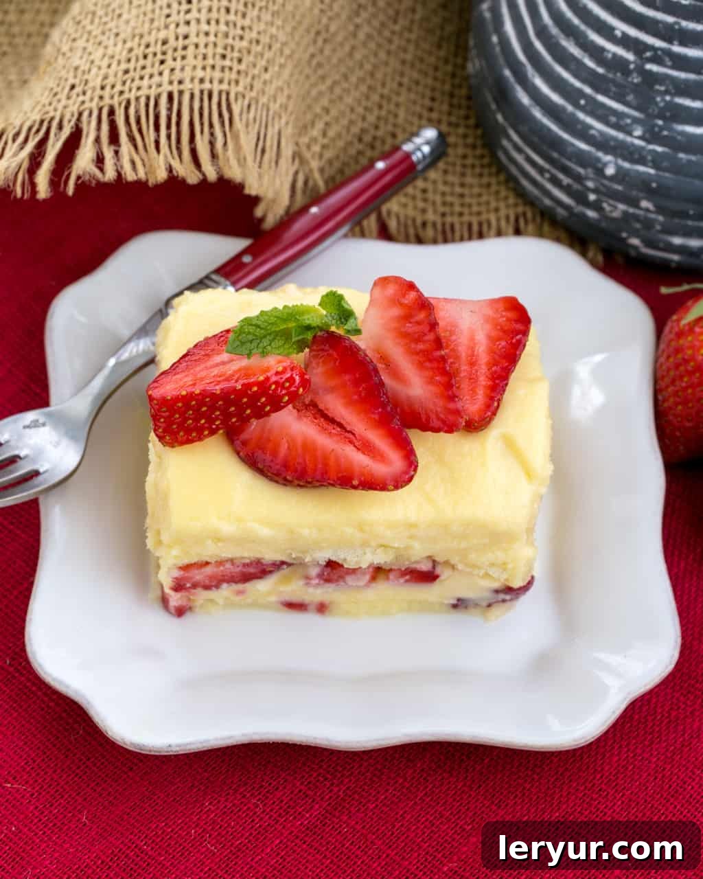Berry Tiramisu with Grand Marnier - A strawberry twist on the Italian classic with mascarpone and Grand Marnier soaked ladyfingers! A slice of Berry Tiramisu with Grand Marnier on a square white plate with a red handled fork, showing layers of cream, ladyfingers, and strawberries.