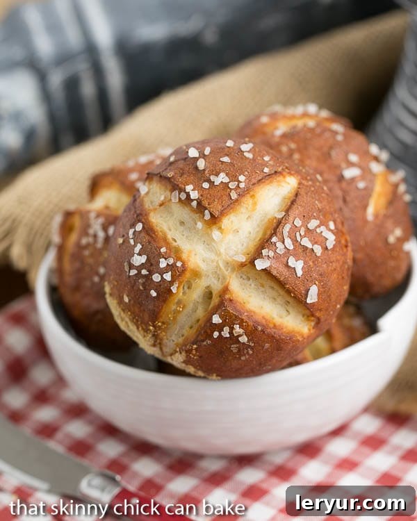 A bowl overflowing with freshly baked, golden brown Homemade Pretzel Rolls, ready to be enjoyed. The soft, pillowy texture and perfectly salted tops are visible.