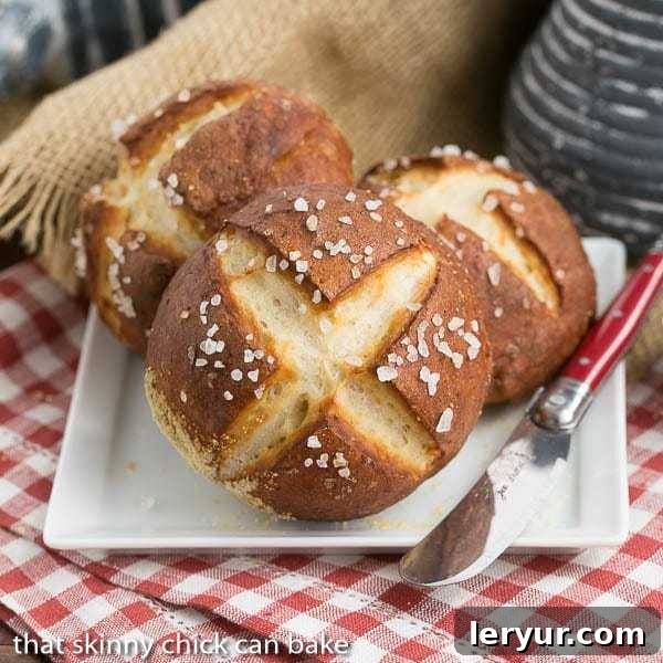 A freshly baked Homemade Pretzel Roll, perfectly golden and scored, rests on a white square plate, inviting you to take a bite. A red-handled knife suggests it's ready to be served.