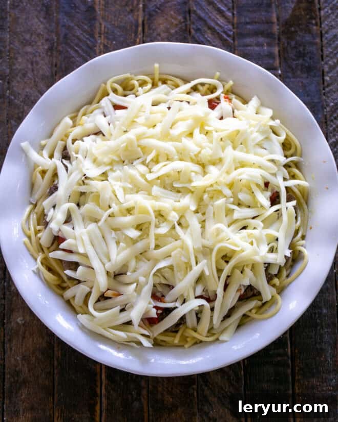 The spaghetti pie generously topped with shredded mozzarella cheese, ready for baking.