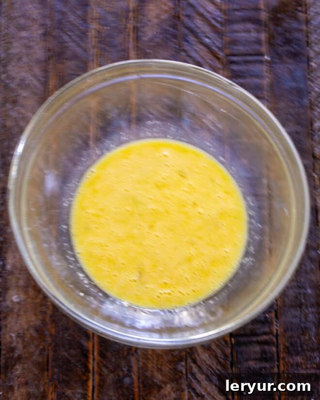 Two eggs beaten with grated Parmesan cheese in a glass bowl, ready to be mixed.