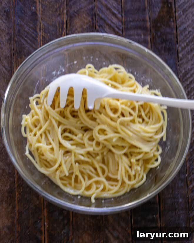 Cooked spaghetti being gently folded into a bowl with beaten eggs and Parmesan mixture.