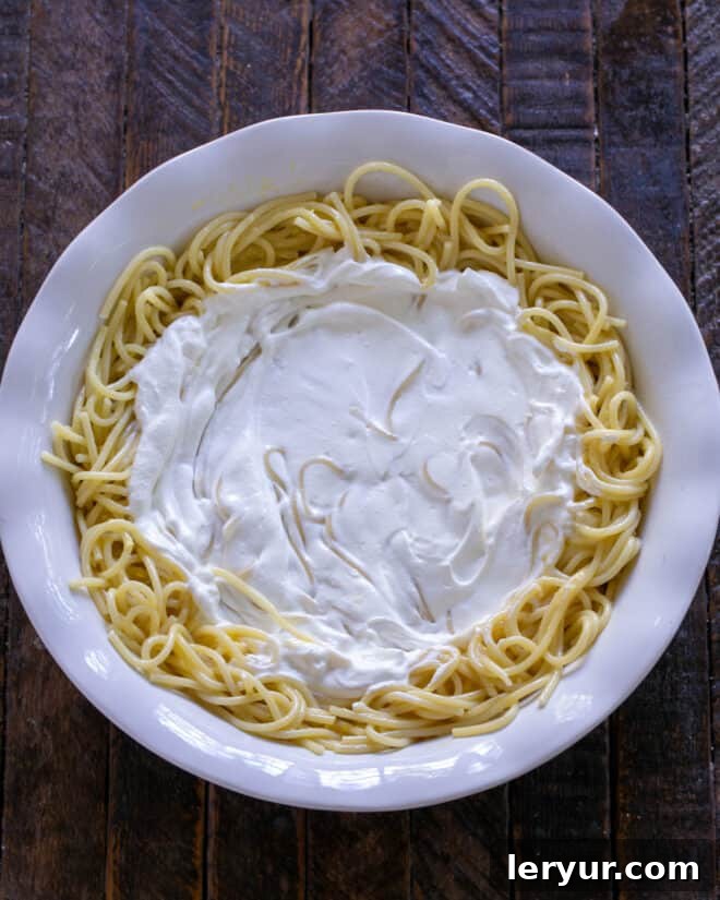 A smooth, even layer of sour cream spread over the spaghetti crust in the pie plate.