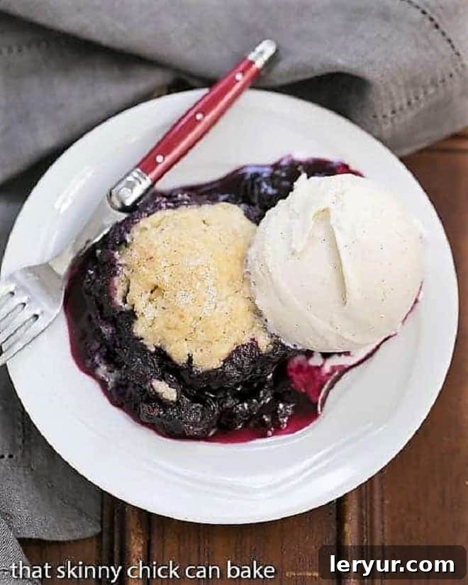 Grilled Blueberry Cobbler - A rustic berry dessert made on the BBQ! Grilled Blueberry Cobbler a la mode on a white plate with a red handled fork.