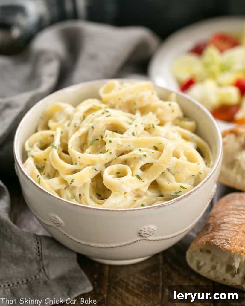 Light Fettuccine Alfredo - A creamy flavorful, lightened up Fettuccine Alfredo that tastes amazing! Light Fettuccine Alfredo in a white bowl with bread and salad in the back ground.