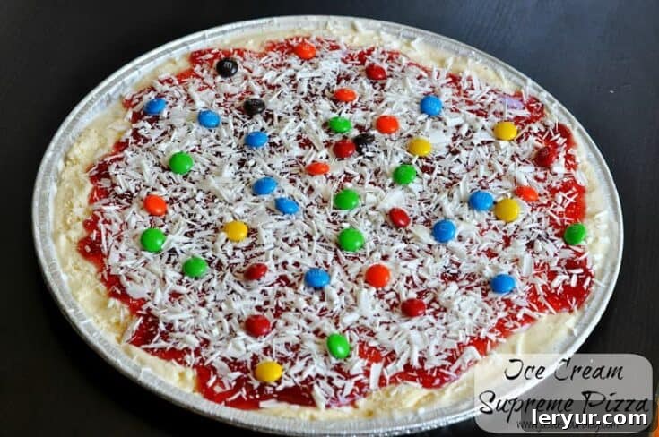 Fun Ice Cream Pizza, topped with various candies, sprinkles, and chocolate drizzles, ready to be sliced.