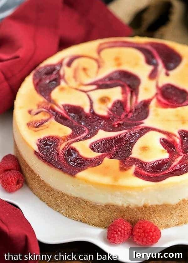 A perfectly sliced White Chocolate Raspberry Swirl Cheesecake on a pristine white plate, elegantly garnished with fresh, vibrant raspberries, showcasing its creamy texture and beautiful fruit swirl.