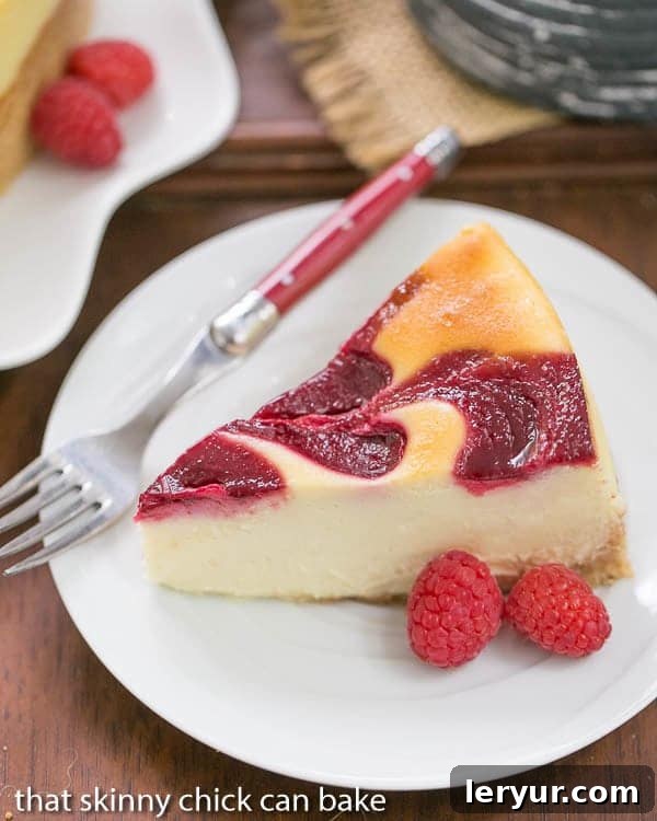 A close-up of a White Chocolate Raspberry Swirl Cheesecake slice, showcasing its delicate raspberry marbling and smooth texture, presented on a white plate with a red-handled fork ready for indulgence.