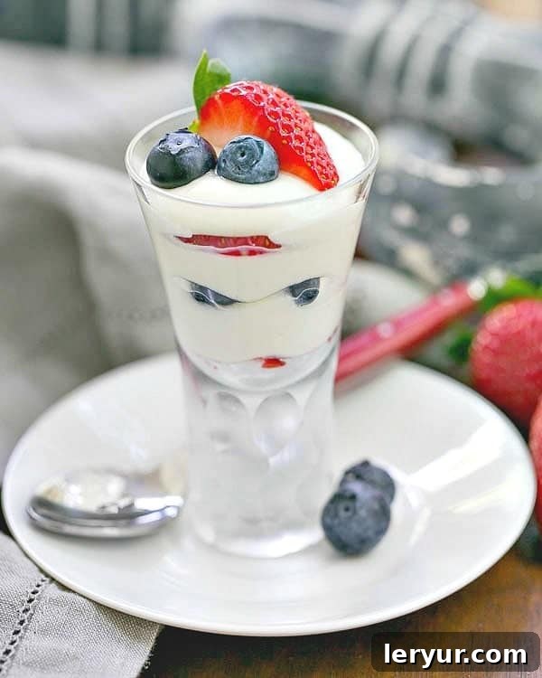 White Chocolate Berry Parfaits - Luscious ripe berries layered with a Frangelico spiked white chocolate mousse Luscious White Chocolate Berry Parfaits on a small white plate with a red handle spoon, showcasing layers of creamy white mousse, fresh strawberries, and blueberries.