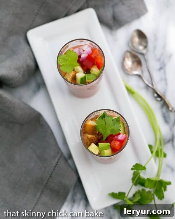 Gazpacho Shooters - Appetizer size portions of the classic Spanish gazpacho recipe Close-up of elegant Gazpacho Shooters arranged on a pristine white rectangular tray, each garnished with a fresh sprig of cilantro, ready to be served.