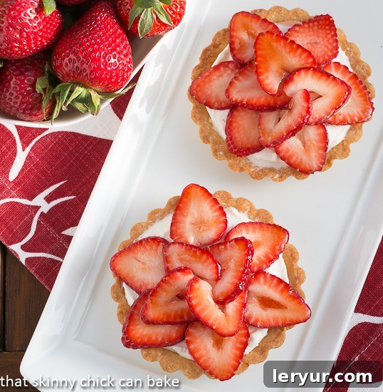 Berry Bliss: 50+ Irresistible Dessert Ideas 4 Artistically arranged Fresh Strawberry Tartlets, gleaming with sliced strawberries over a creamy filling.