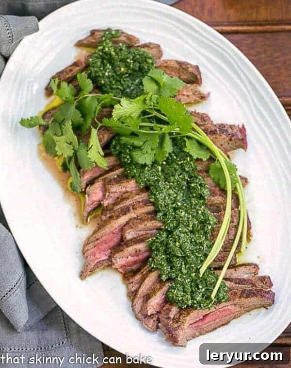 Overhead view of perfectly grilled Flank Steak adorned with vibrant Chimichurri Sauce, presented on an elegant white oval platter.