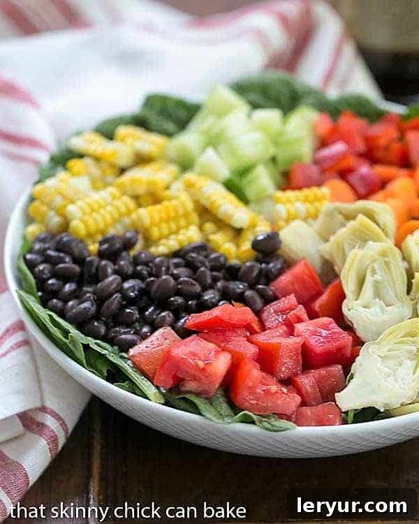 A vibrant composed Summer Vegetable Salad, showcasing fresh spinach topped with a rainbow of colorful vegetables in a white serving bowl.