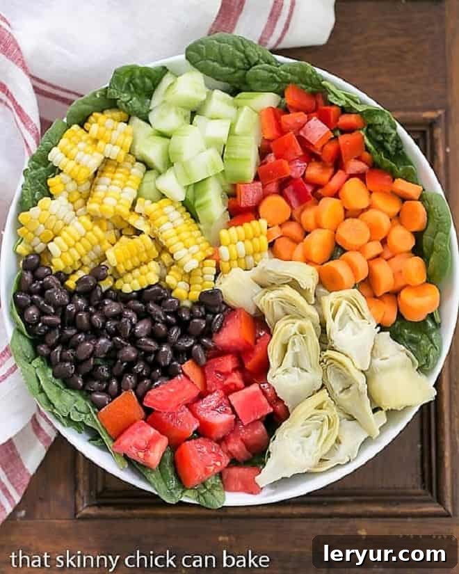 An overhead shot of a beautifully composed Summer Vegetable Salad, meticulously arranged in sections within a white serving bowl, showcasing a rainbow of fresh ingredients.