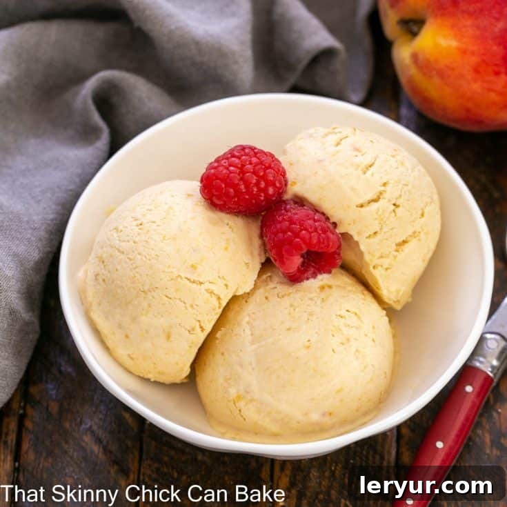 3 scoops of peach ice cream in a white ceramic bowl with 2 fresh raspberries