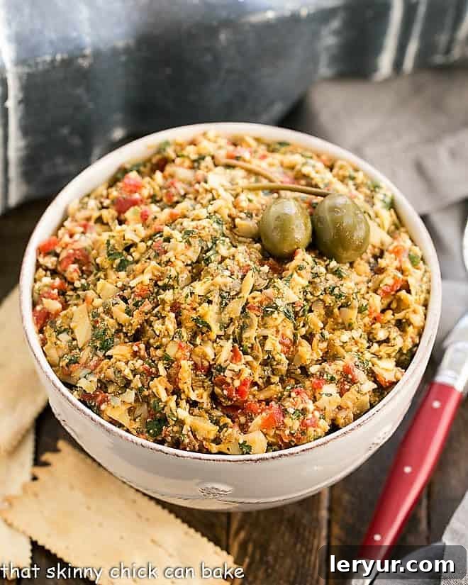 Red Pepper Artichoke Tapenade - a marvelous Artichoke Dip Recipe that's fabulous served with crackers or fresh vegetables An overhead shot showcasing the textured Roasted Red Pepper Artichoke Tapenade in a rustic white bowl, with a red-handled spoon resting on the side, inviting you to scoop and savor.