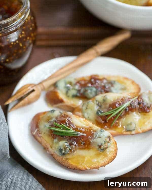Fig Gruyere Crostini - An unusual combination of toppings that's sure to be a hit! Fig Gruyere Crostini on a white appetizer plate with a wooden honey drizzler.