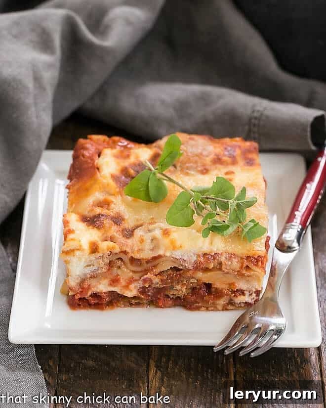 A slice of Lasagna with Italian Sausage on a white plate, served with a red handled fork.