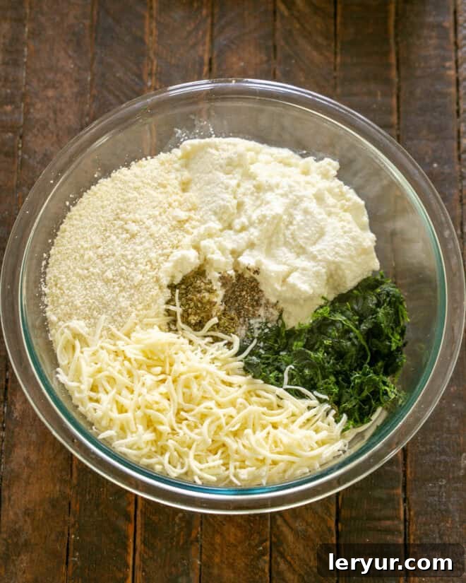 Mixing bowl with ricotta cheese, shredded mozzarella, grated Parmesan, eggs, dried oregano, salt, black pepper, and thoroughly squeezed dry spinach, ready to be combined into a creamy filling.