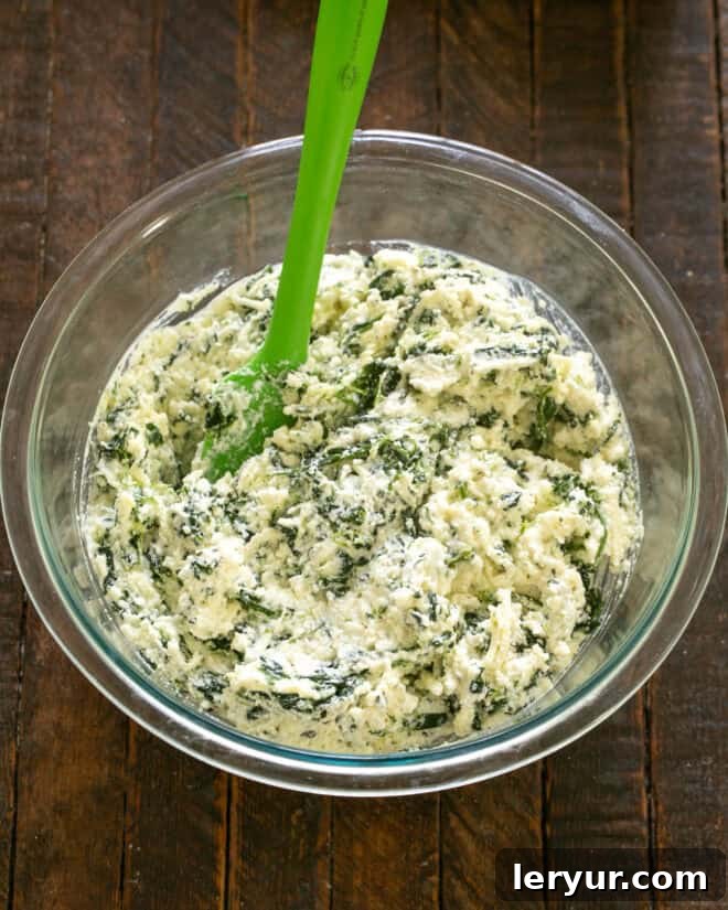 Cooked jumbo pasta shells being carefully filled with the rich spinach and ricotta mixture using a spoon or small scoop, demonstrating the stuffing technique.