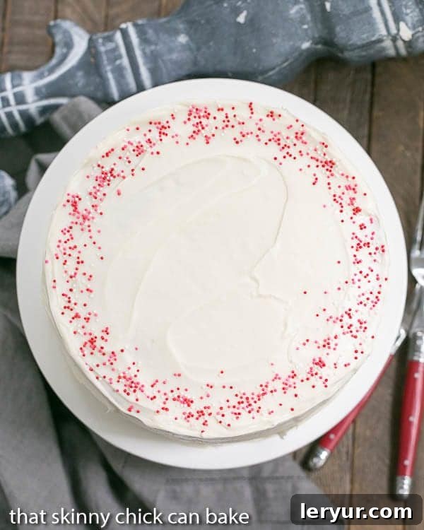 Red Velvet Checkerboard Cake - A showstopper of a celebratory cake! An assembled Red Velvet Checkerboard Cake adorned with cream cheese frosting, presented on a white cake plate.