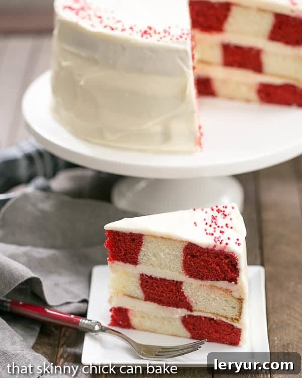 Crimson Checkered Delight 2 A close-up view of a slice of Red Velvet Checkerboard Cake, showing the vibrant red and white squares, with the whole cake blurred in the background on a cake stand.