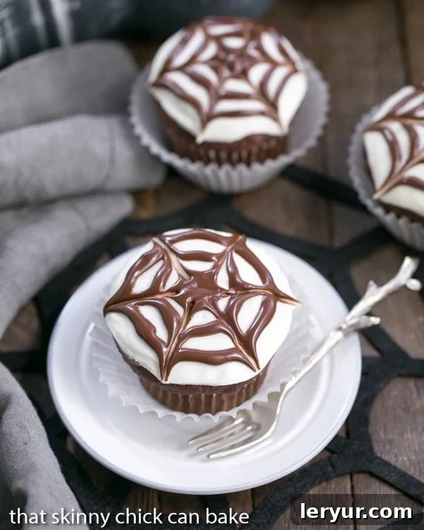 One Spiderweb Cupcake on a white plate with 2 in the background, ready for Halloween.