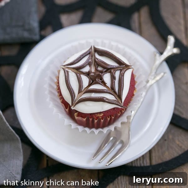 A perfectly decorated Spiderweb Cupcake on a small white plate, ready for Halloween.