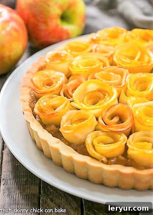 A beautifully arranged Rosette Apple Tart on a pristine white plate, showcasing its intricate apple rose topping and golden crust.